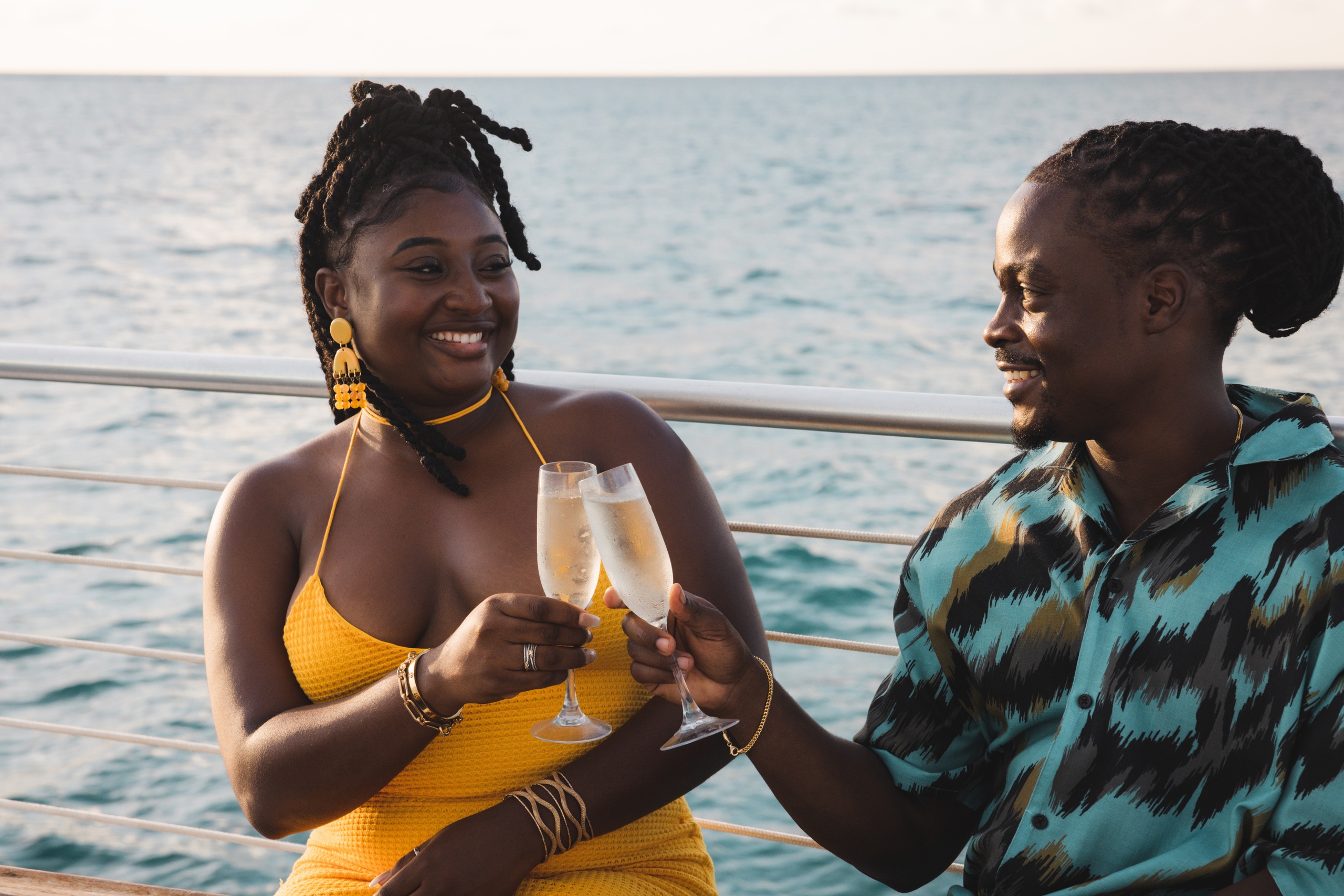 A couple on a boat toasting with champagne glasses against a sea backdrop.
