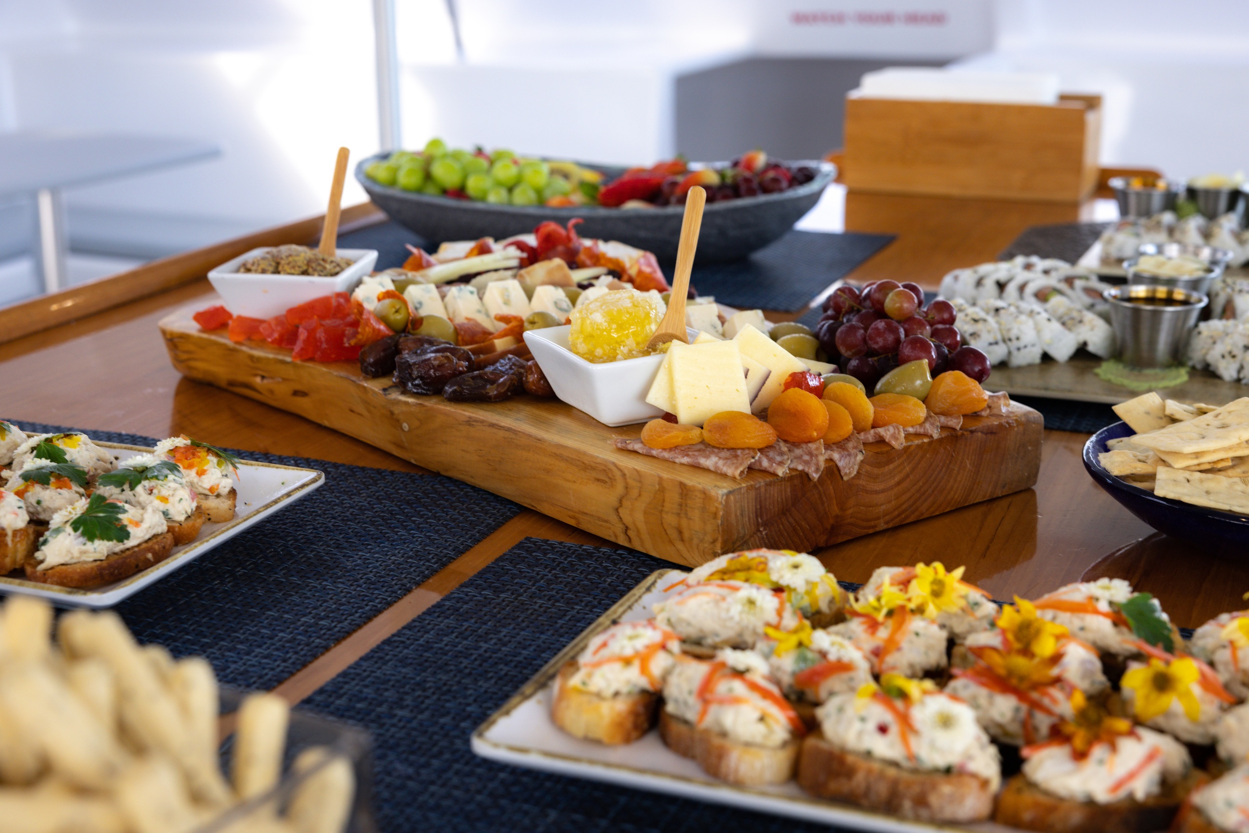 Variety of appetizers on wooden board and plates, including cheeses, fruits, and garnished bread slices.