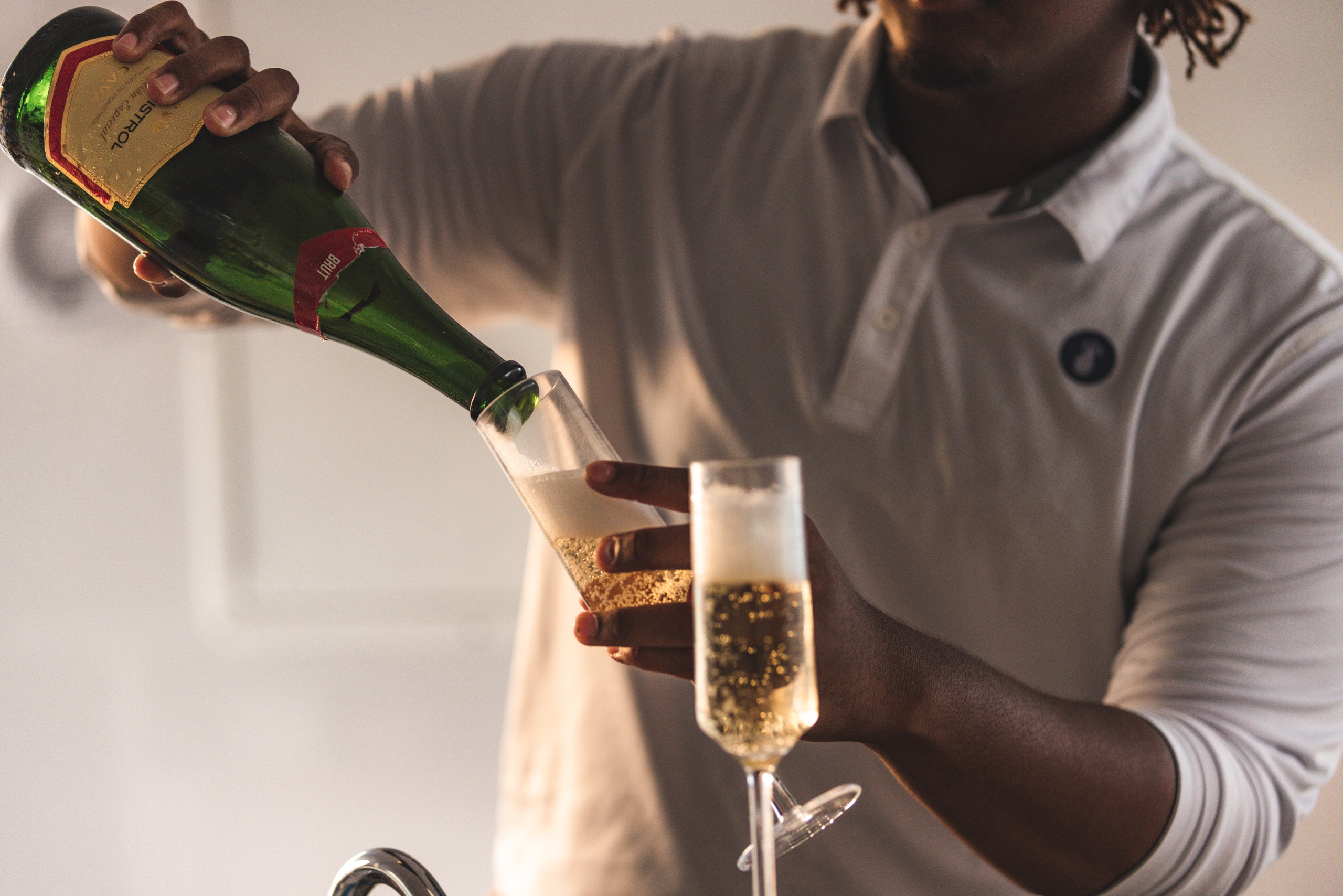 Person in a white shirt pouring champagne into a flute glass.