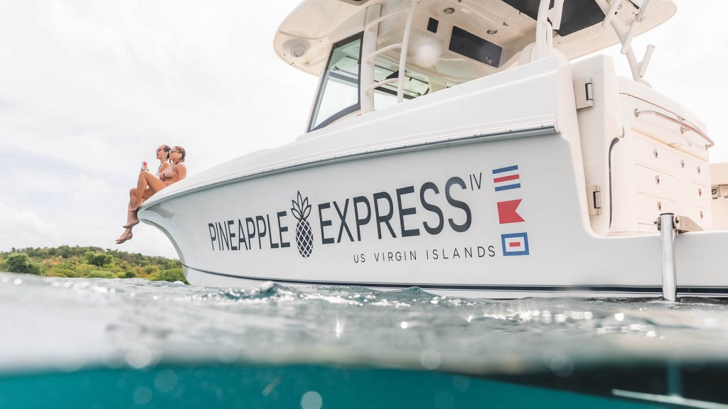 Boat named Pineapple Express on water, with two people sitting on the edge.