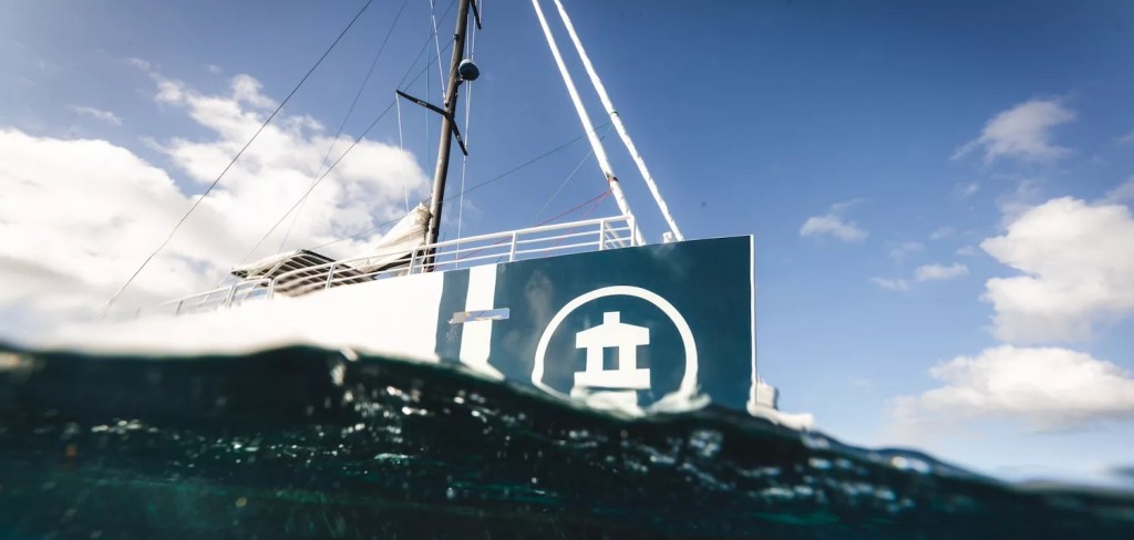 Partial view of a ship's hull above water, with logo and sky in the background.