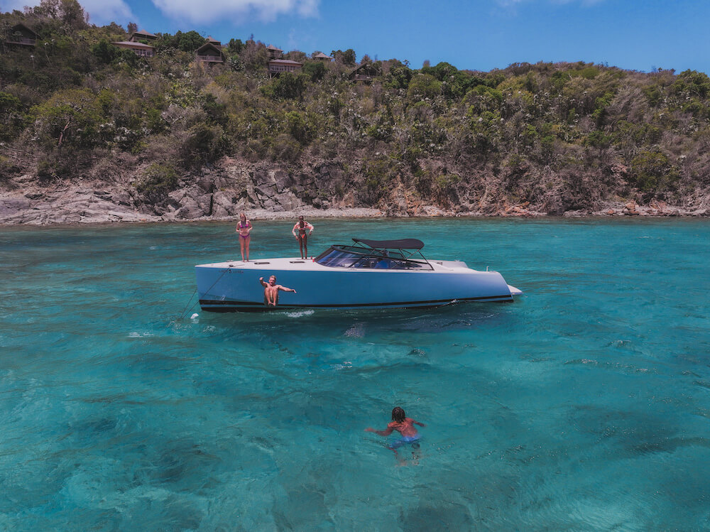Boat with people floating in clear blue water near a rocky shoreline.