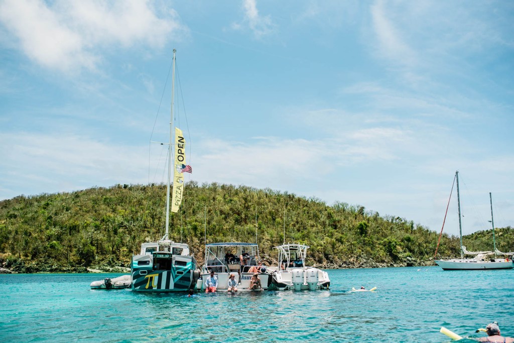 Boats anchored near an island in clear blue water under a partly cloudy sky.