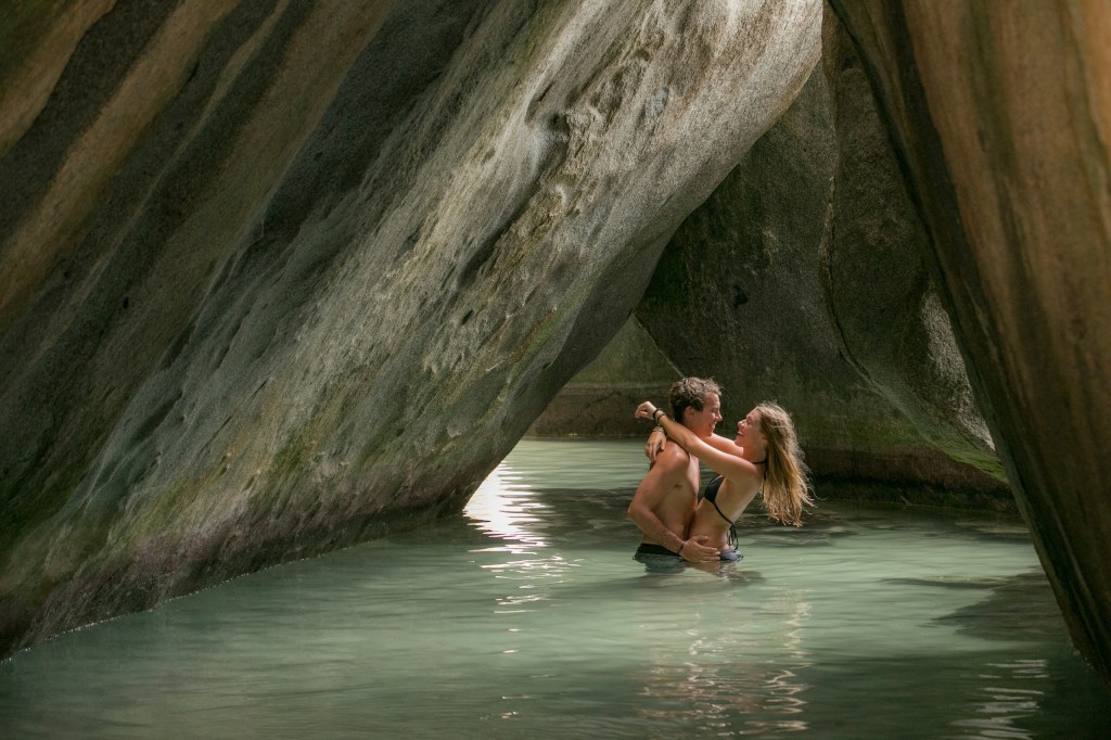 A couple embracing in water under a rocky archway.