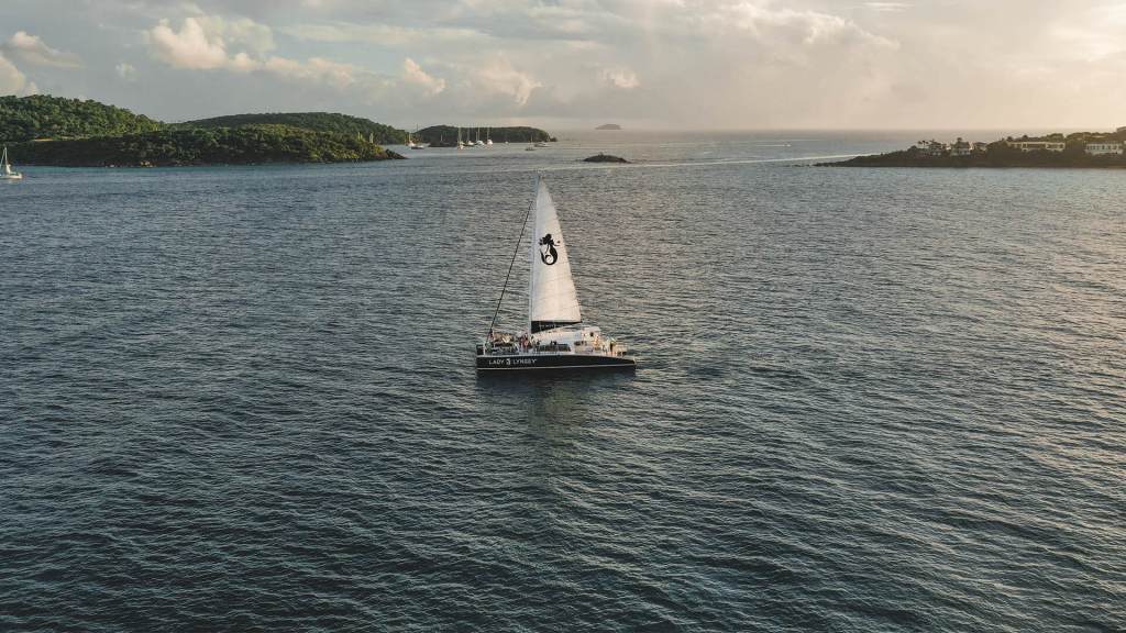 Sailboat on open water with distant islands and cloudy sky.