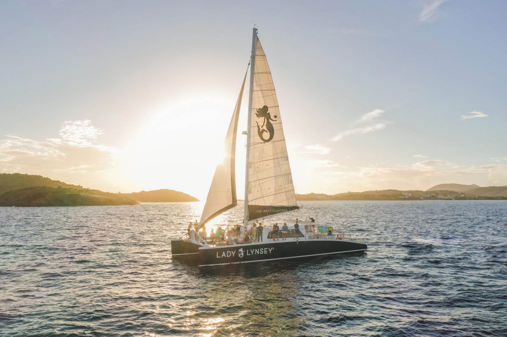 Sailboat on ocean at sunset with hilly islands in the background.