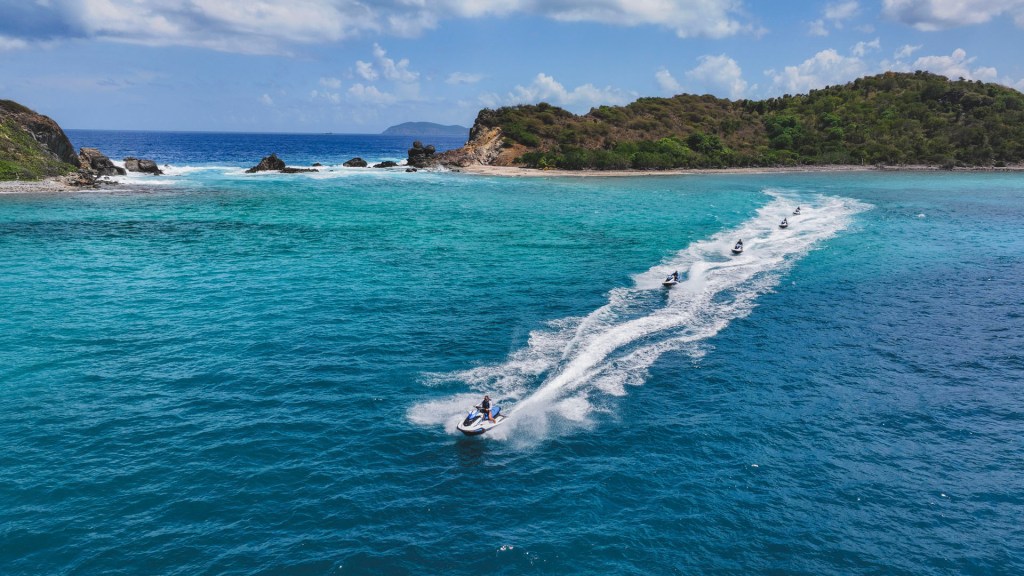 Multiple jet skis creating waves on clear turquoise water near a small island.