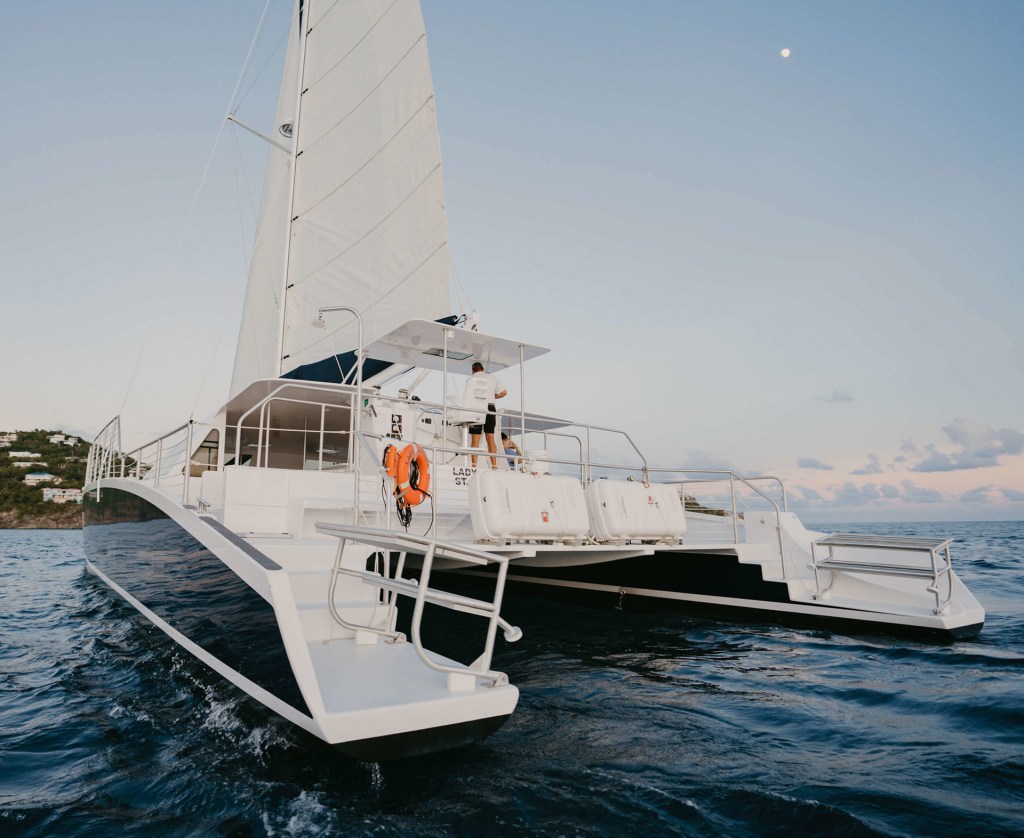Sailboat on calm ocean at sunset with moon in the sky.