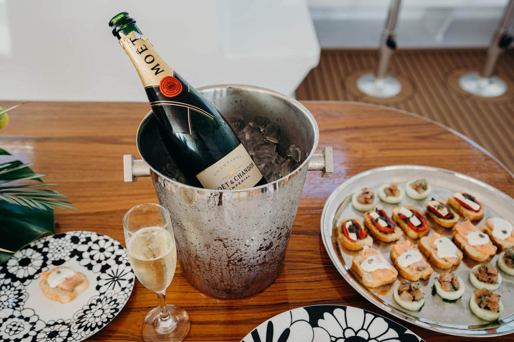 Champagne bottle in ice bucket with appetizers on a table.