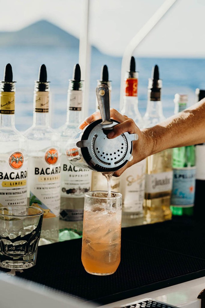 A hand pouring a cocktail into a glass with Bacardi bottles in the background.