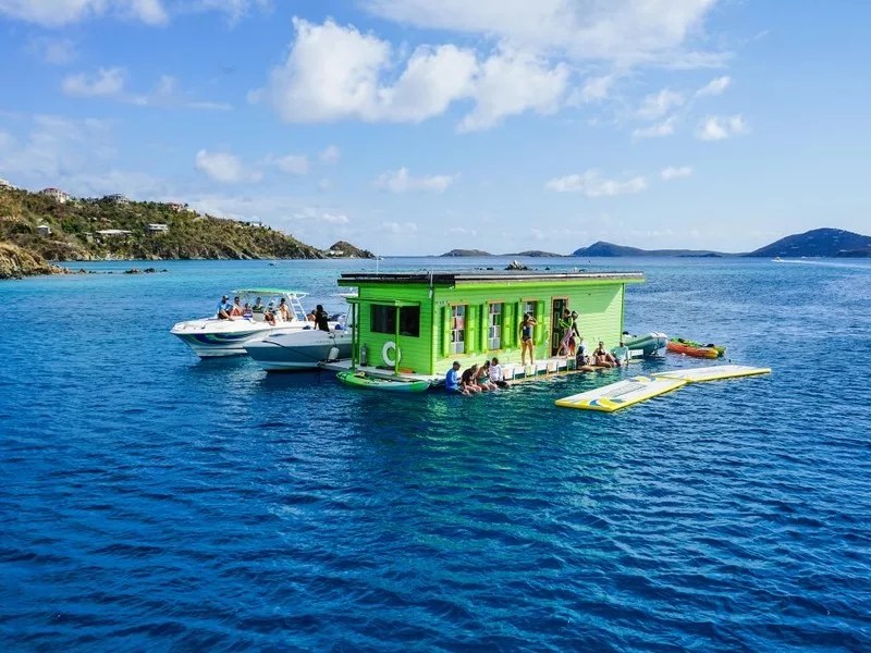 Bright green floating bar with people and boats around, in clear blue water.
