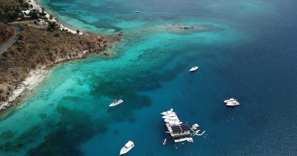 Aerial view of a coastline with boats anchored near a floating platform in clear turquoise water.