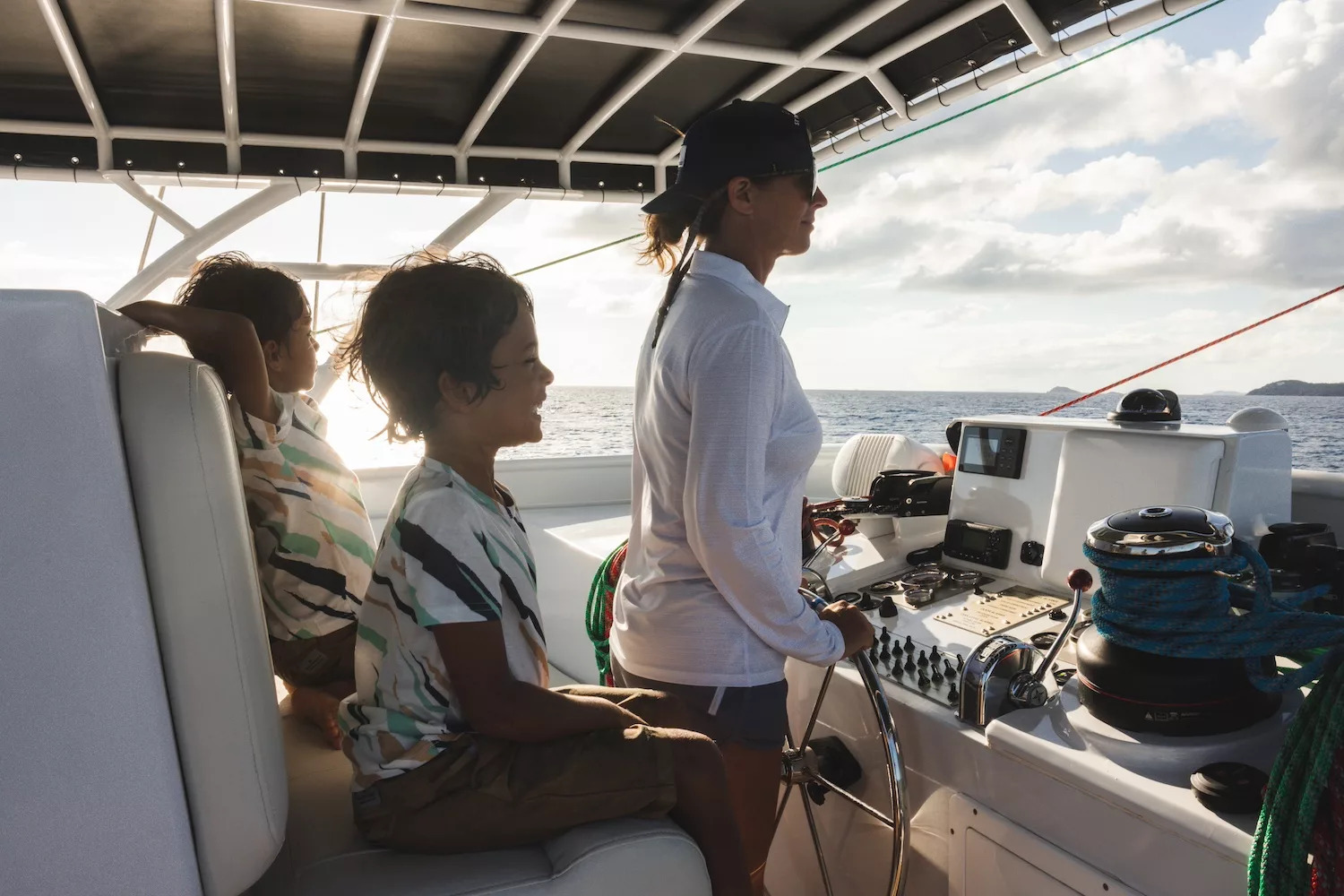 Woman steering boat with two children seated beside her, under a canopy on a sunny day.