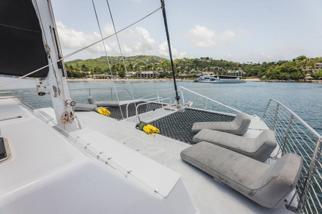 Deck of a yacht with gray lounge chairs, overlooking a calm sea and distant shoreline.