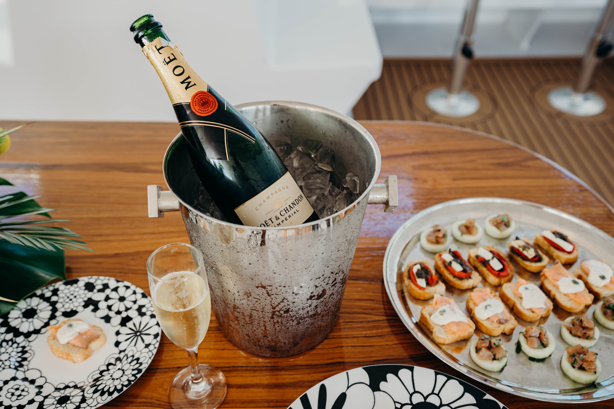 Champagne bottle in ice bucket with glass and appetizers on wooden table.