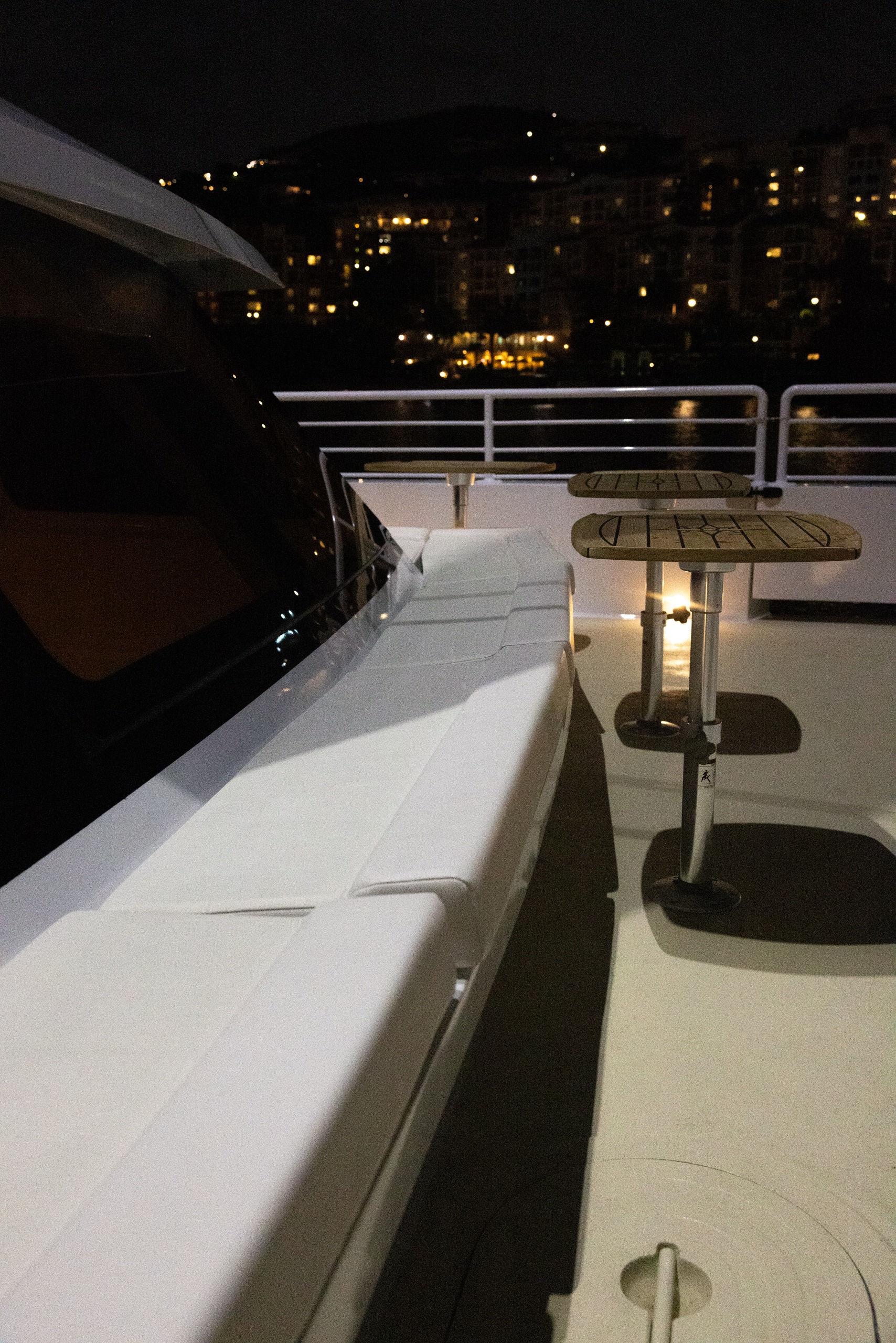 Outdoor yacht deck with tables and seating at night, city lights in background.