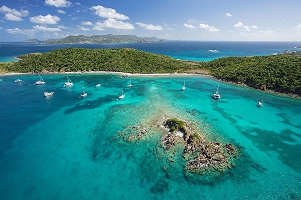 Aerial view of turquoise waters with boats near a small island, surrounded by lush greenery and distant land.