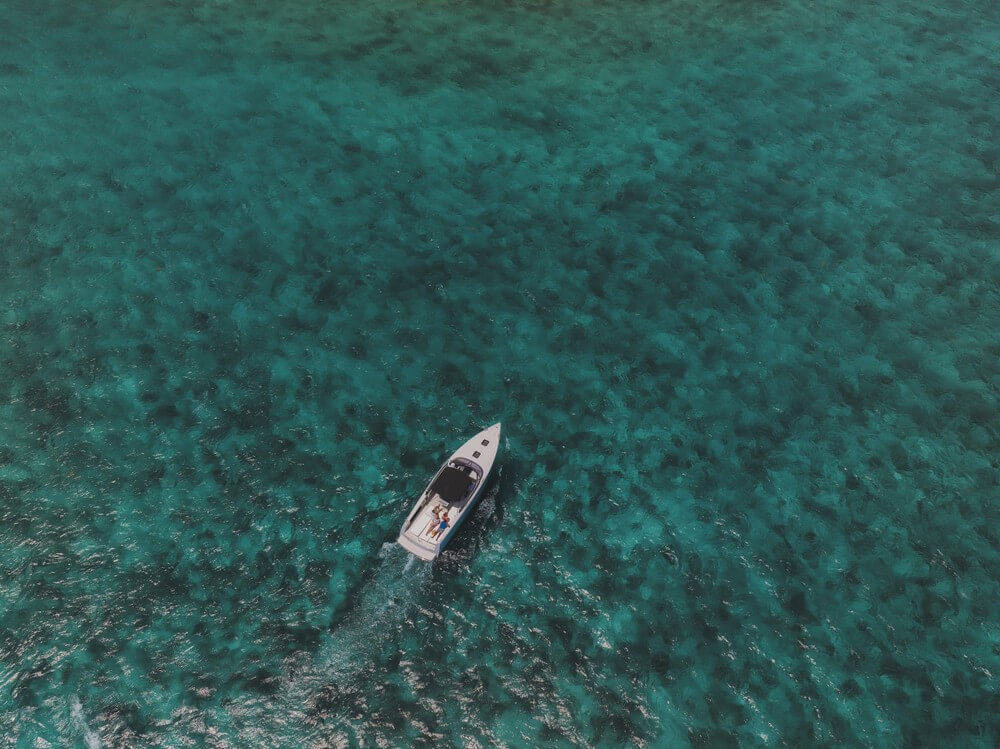 Aerial view of a small boat sailing on clear turquoise water.
