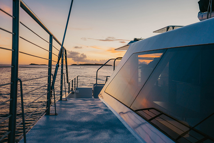 Catamaran deck overlooking ocean at sunset with railing and windows visible.