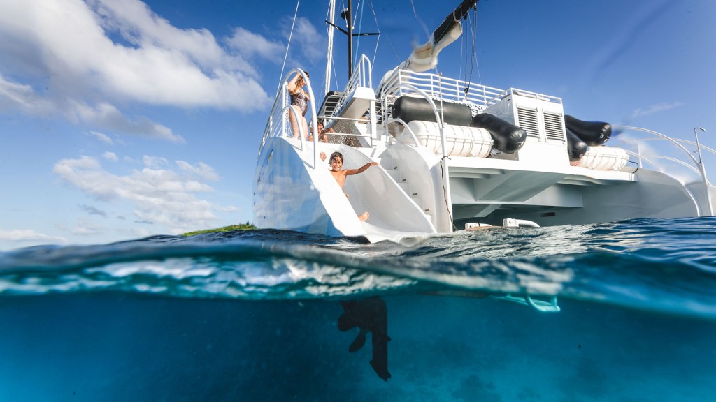 View of a catamaran on water with a person diving in, partly submerged perspective.
