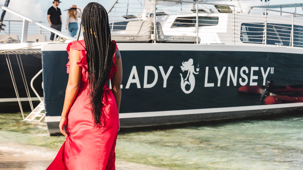 Woman in red dress stands by boat named 'Lady Lynsey' at dock with clear water.