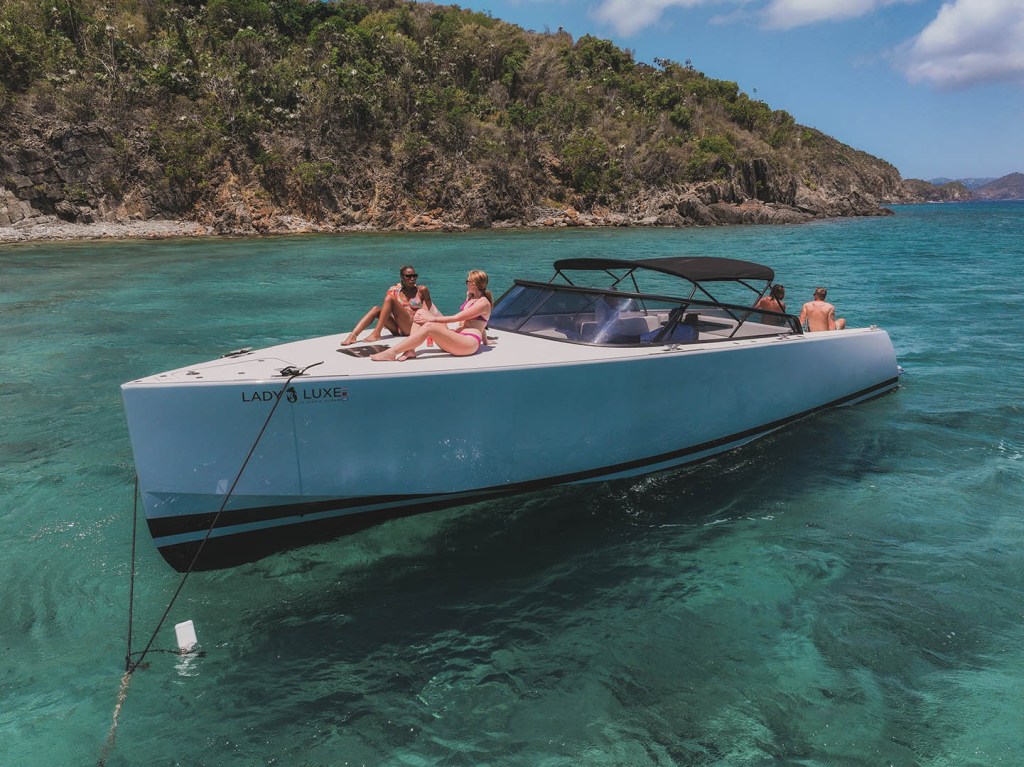 People relaxing on a boat in clear turquoise water near a tropical island.
