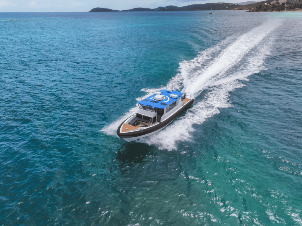 Motorboat with blue canopy traveling fast in clear blue ocean near coast.