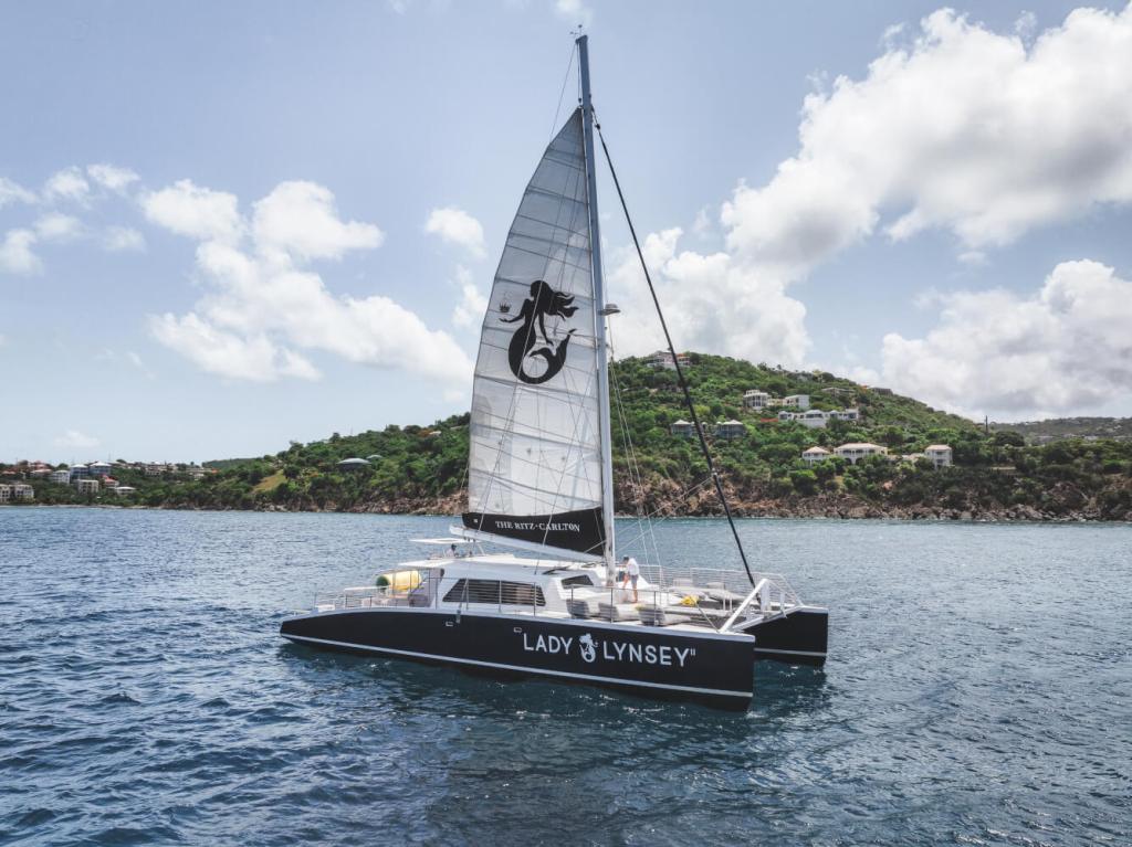 Sailboat named Lady Lynsey in calm waters near a hilly coastline under a partly cloudy sky.