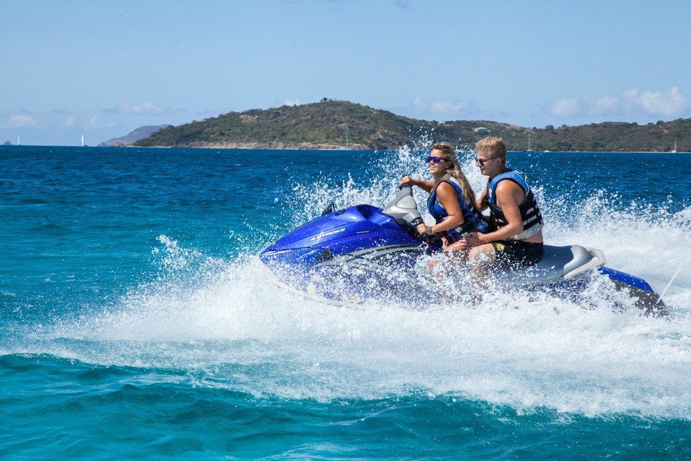 Two people riding a jet ski on the ocean with an island in the background.