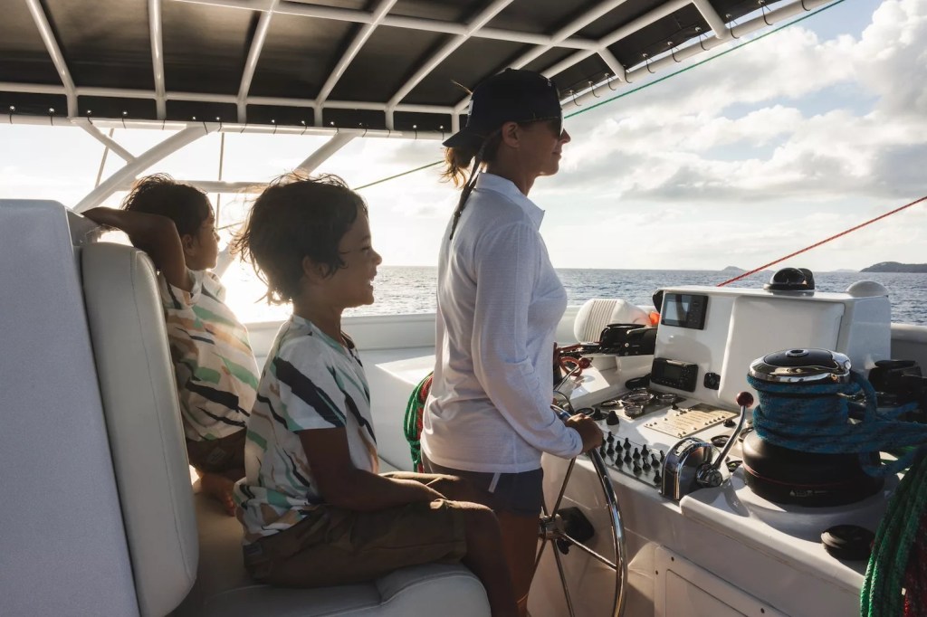 Person steering a boat with two kids seated on a sunny day.