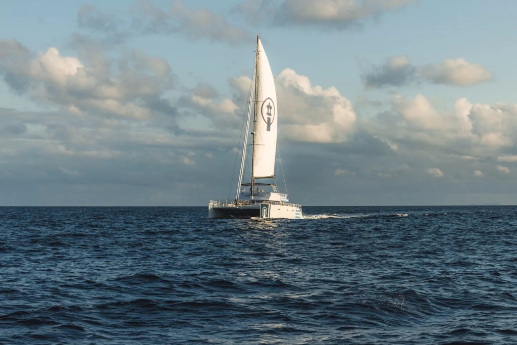 Sailboat with white sail on a calm sea under a partly cloudy sky.