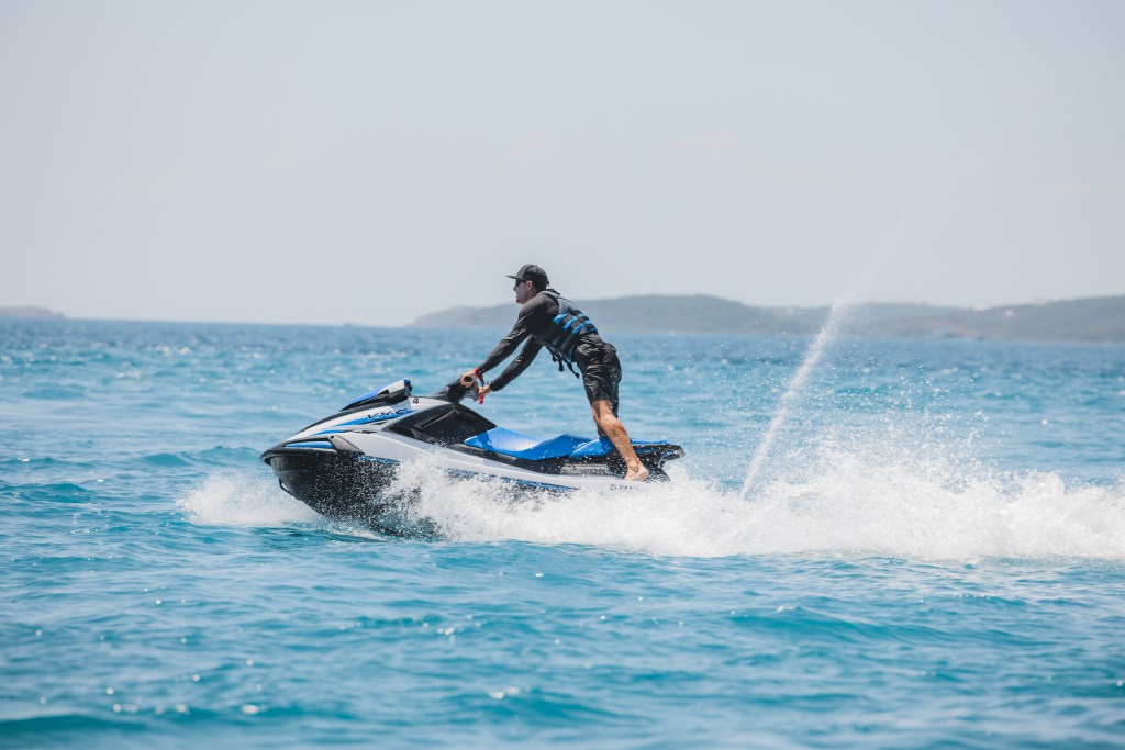 Person riding a jet ski on the ocean with distant land visible in the background.