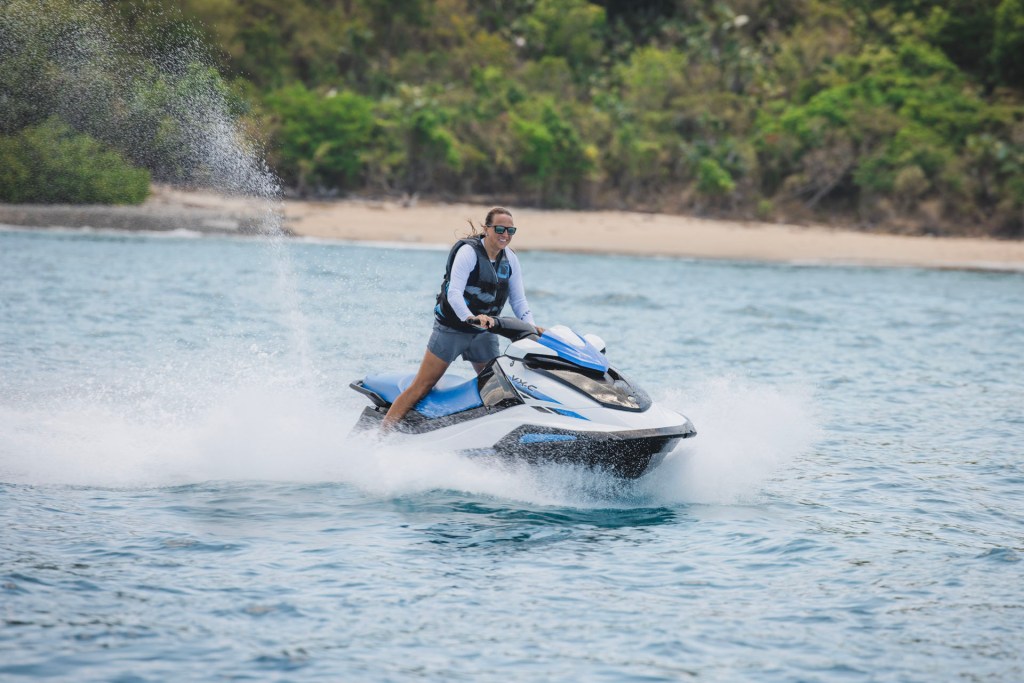 Person riding a jet ski on the ocean near a beach with trees.