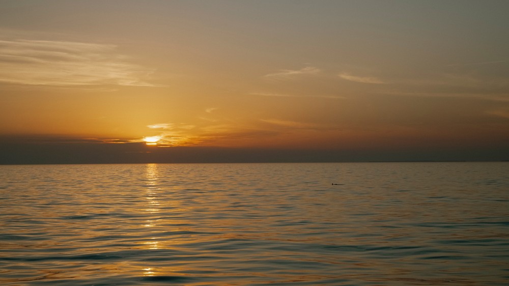 Calm ocean at sunset with orange hues and a cloudy sky.
