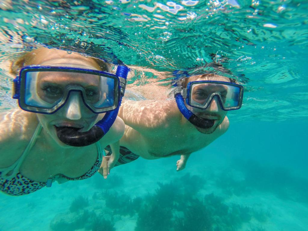 Two people snorkeling underwater with blue masks in clear ocean water.