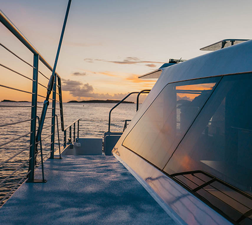 Boat deck overlooking calm sea at sunset with railing and cabin reflections.