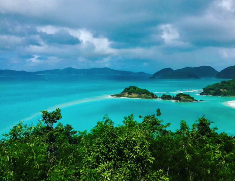 Tropical island with turquoise water and lush greenery under a cloudy sky.