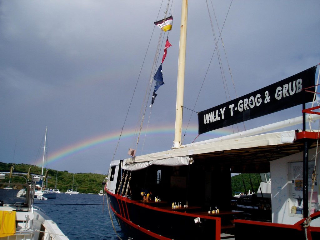Boat with 'Willy T-Grog & Grub' sign docked, rainbow in cloudy sky.