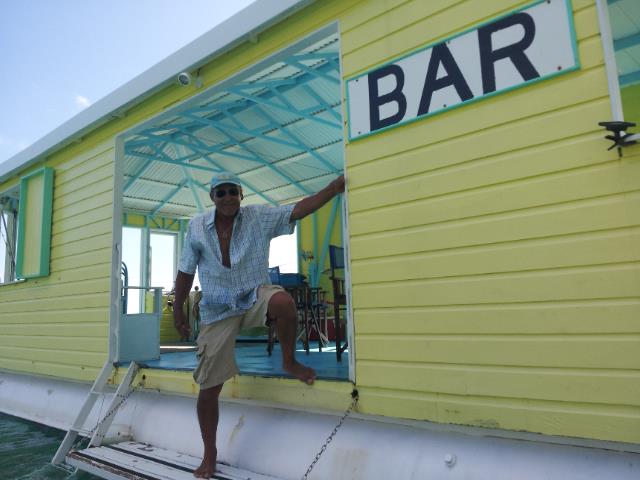 Man standing in doorway of yellow floating bar on water.