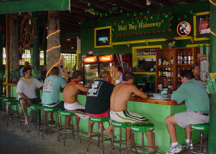 People seated at a bar counter in a tropical-themed bar with green decor and wooden elements.