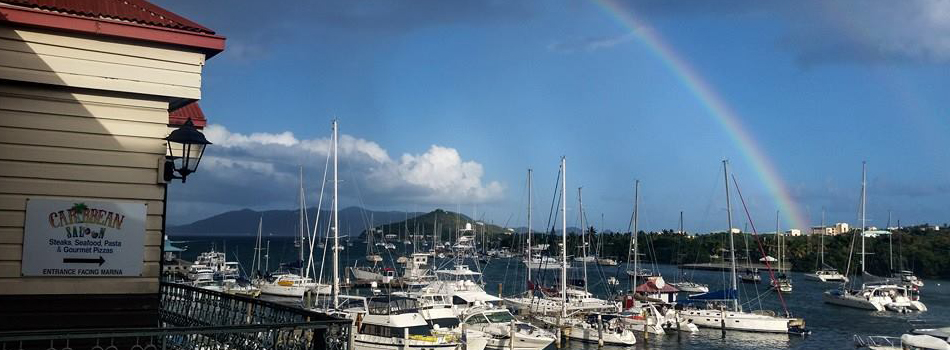 Marina with sailboats and a rainbow in the sky on a sunny day.