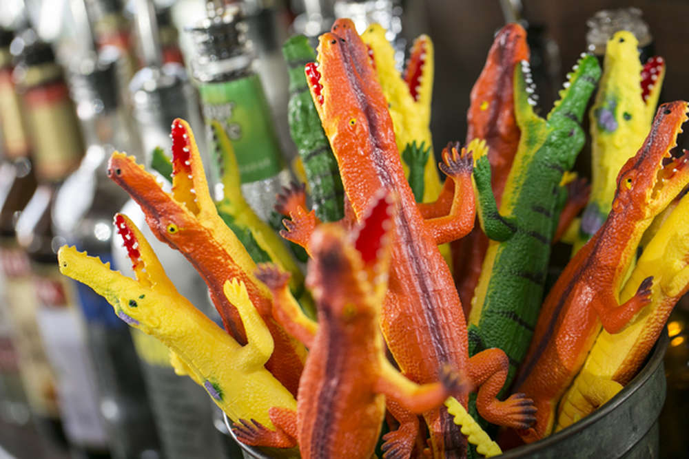 Colorful rubber alligator toys in a container near bottles on a shelf.