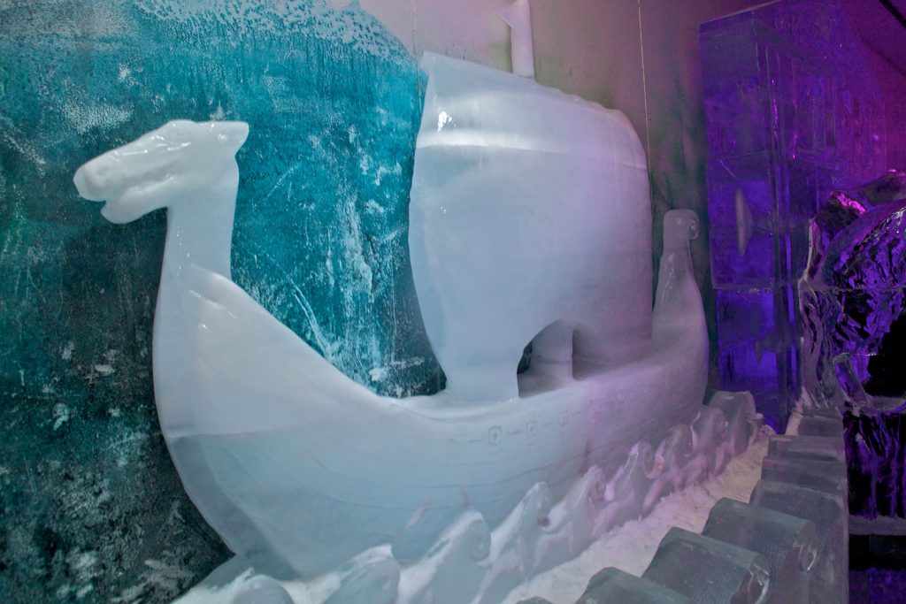 Ice sculpture of a Viking ship with sail, surrounded by blue and purple lighting.