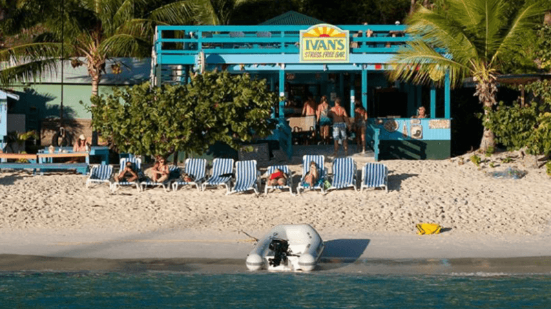 Beachfront bar with lounge chairs, people relaxing, and a small boat near the shore.