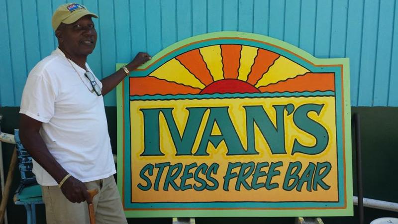 Man standing beside sign for Ivan's Stress Free Bar with colorful sunrise design.
