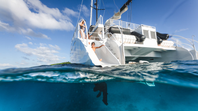 Person sliding off yacht into clear blue water under a sunny sky.