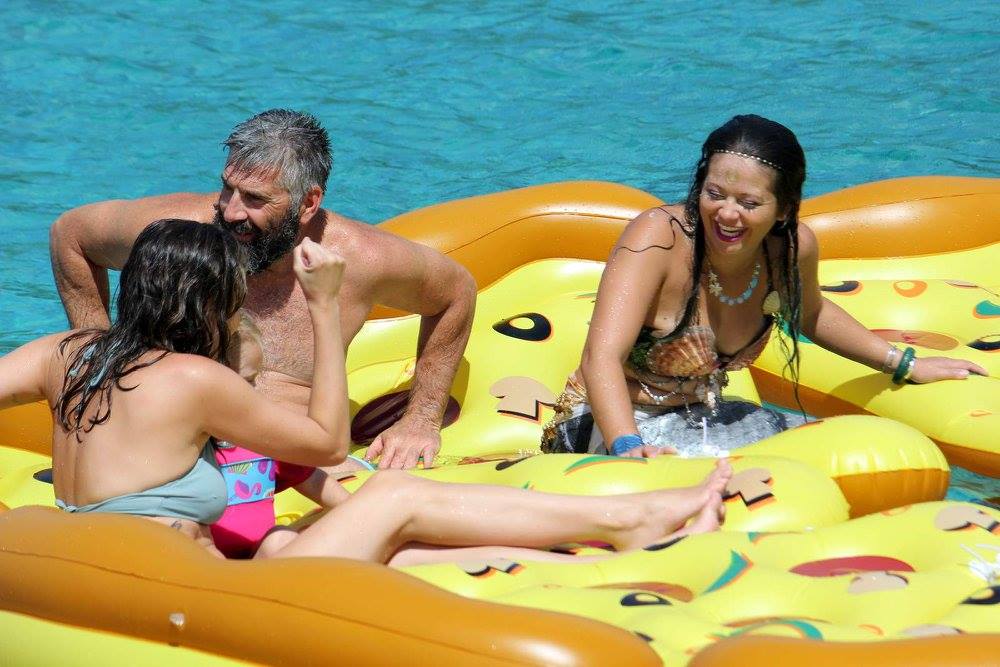 Three people on a pizza-shaped float in a pool, smiling and enjoying the water.