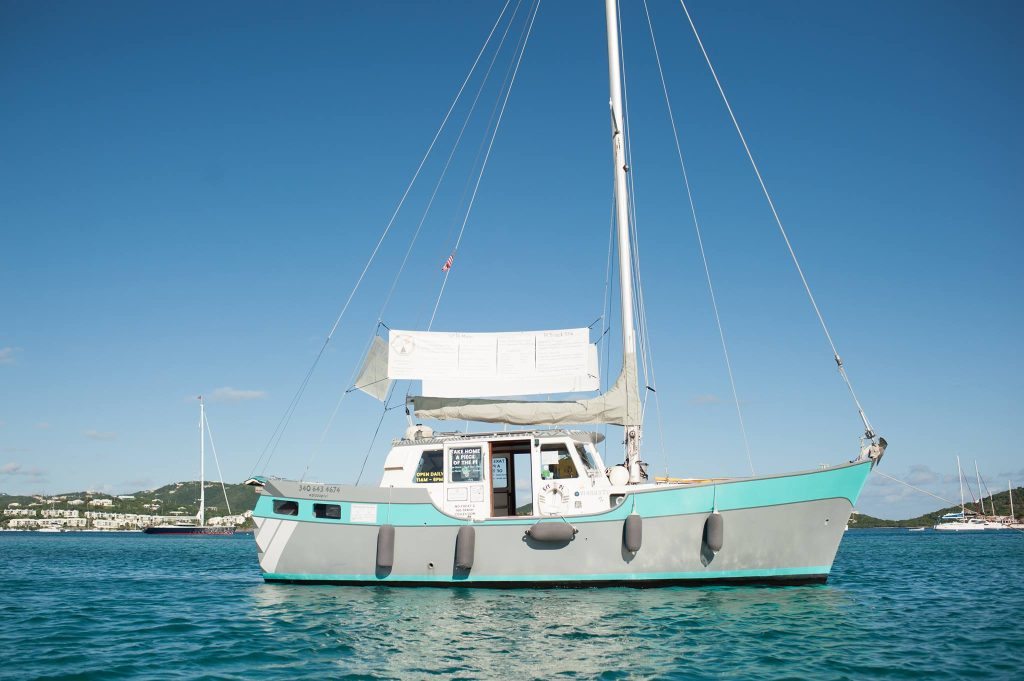 Small sailboat with a turquoise hull moored on calm blue water under a clear blue sky.