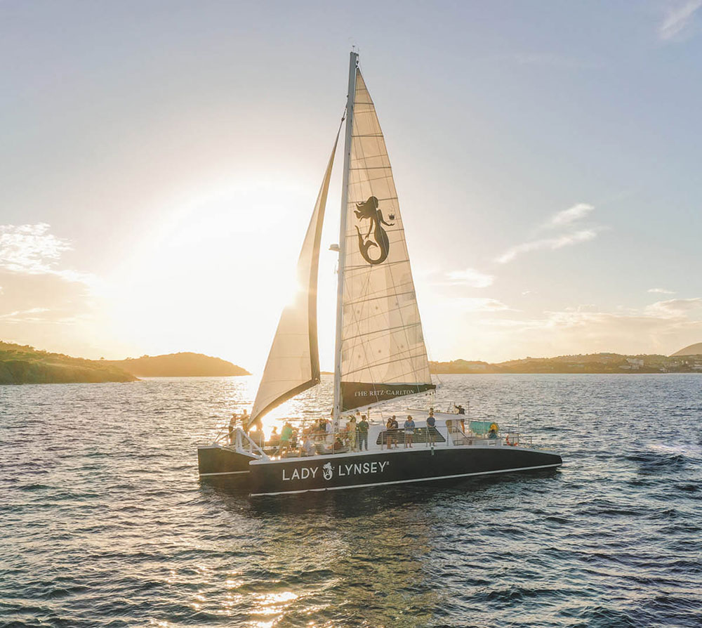 Catamaran labeled 'Lady Lynsey' sailing at sunset with visible passengers.