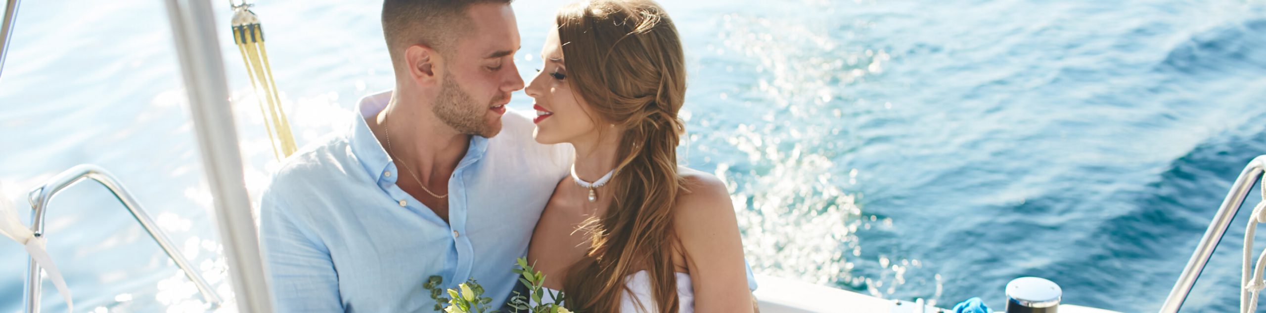 Couple on a boat embracing, holding drinks, with ocean in background.
